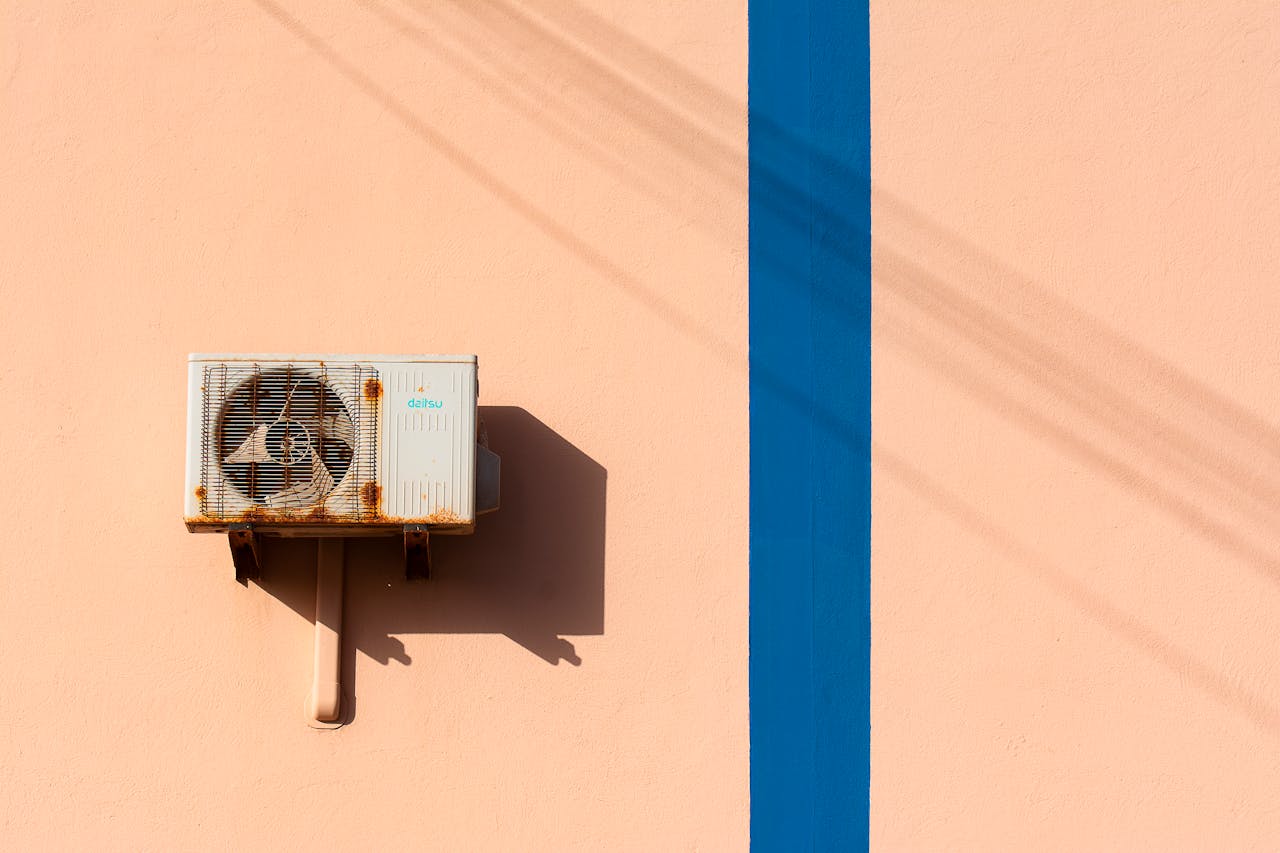 Rusty air conditioning unit casting shadow on a peach wall with blue stripe.