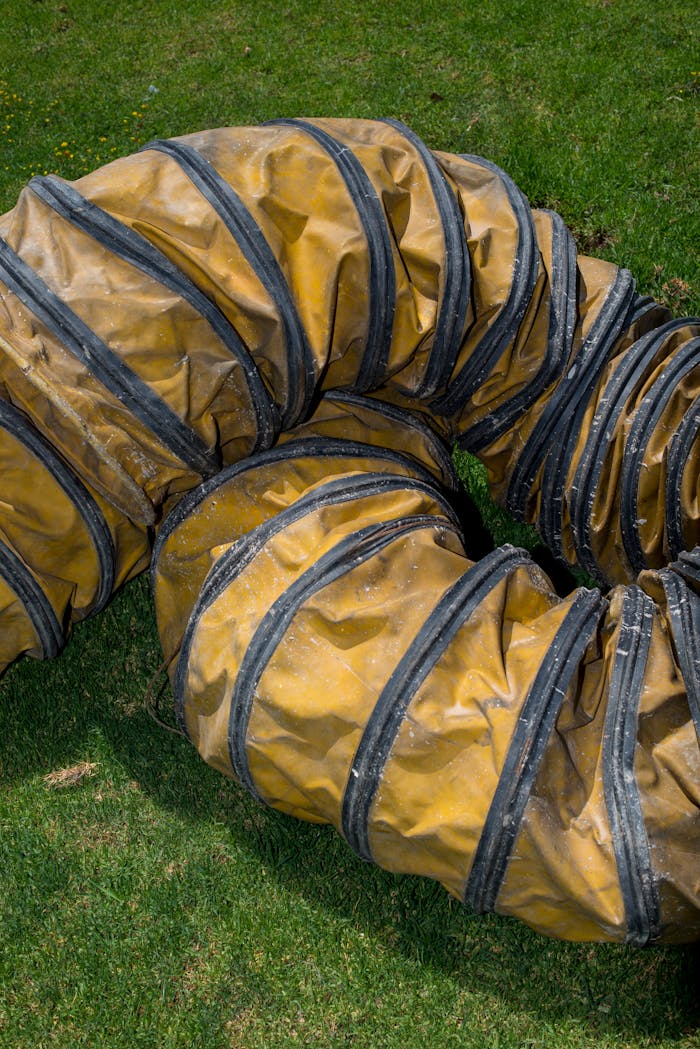 Close-up of a coiled yellow industrial ventilation duct resting on green grass.